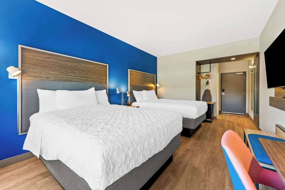 A hotel room with two beds, a desk, a chair, and a TV.