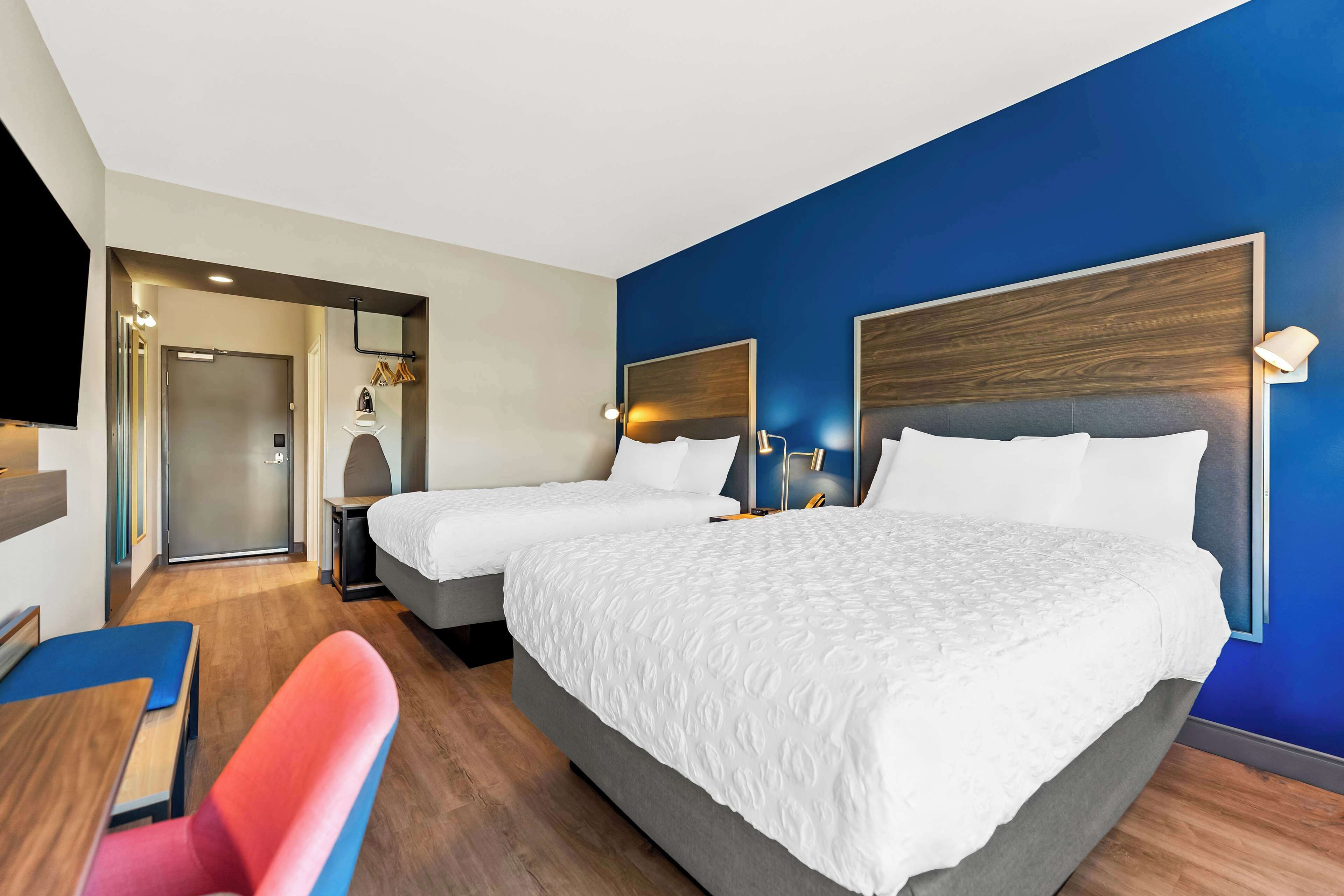 A hotel room with two beds, a desk, a chair, and a TV.