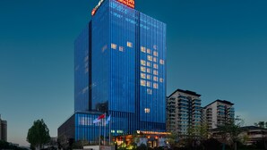 A modern Hilton Garden Inn hotel with a prominent glass facade, surrounded by other buildings and a well-maintained garden area. - Hilton Garden Inn Fenyang Yulongwan (Lvliang)