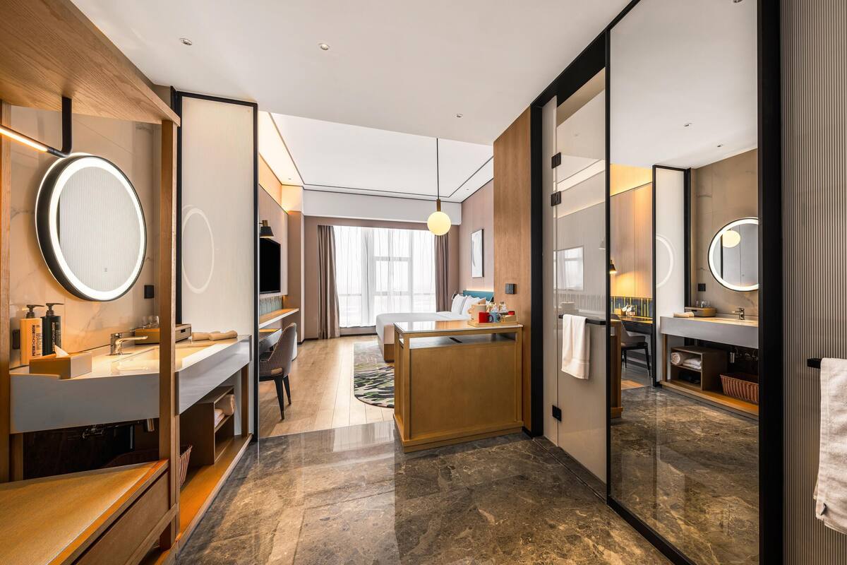 Een moderne hotelkamer met een bed, een bureau, een badkamer met spiegel en een groot raam.
