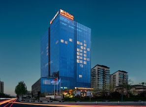 Un hotel moderno con un letrero llamativo, rodeado de otros edificios y un jardín bien cuidado.