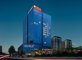 Un hotel moderno con un letrero llamativo, rodeado de otros edificios y un jardín bien cuidado.