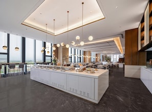 Un espace de restauration moderne dans un hôtel, avec un îlot central, des luminaires suspendus et de grandes fenêtres offrant une vue panoramique.