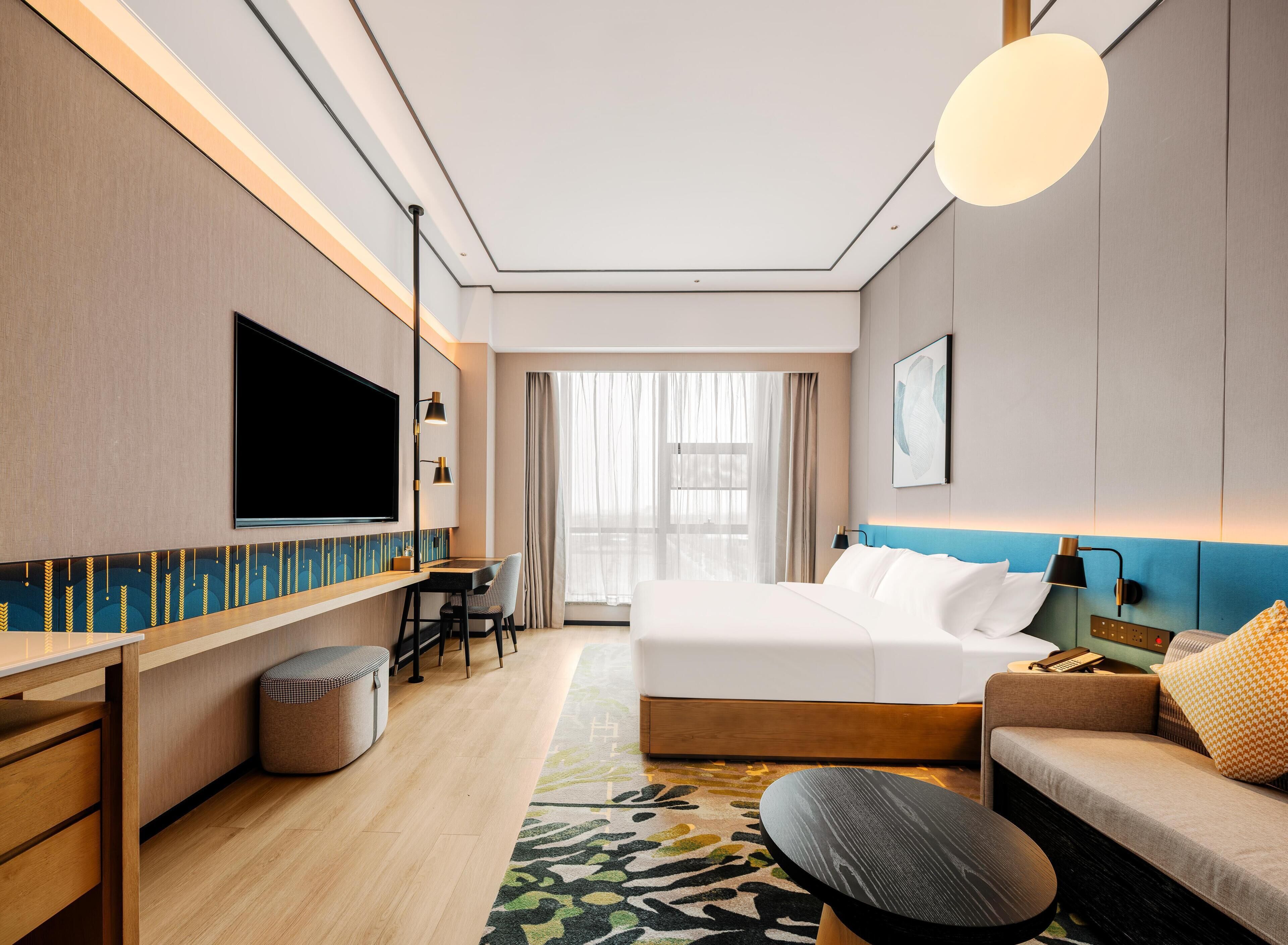 Ein modernes Hotelzimmer mit einem großen Bett, einer Sitzecke, einem Schreibtisch und einem Fernseher.