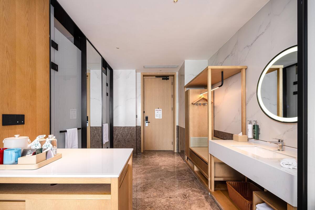 Een moderne hotelbadkamer met een wastafel, spiegel, handdoekrek en een klein tafeltje met toiletartikelen.
