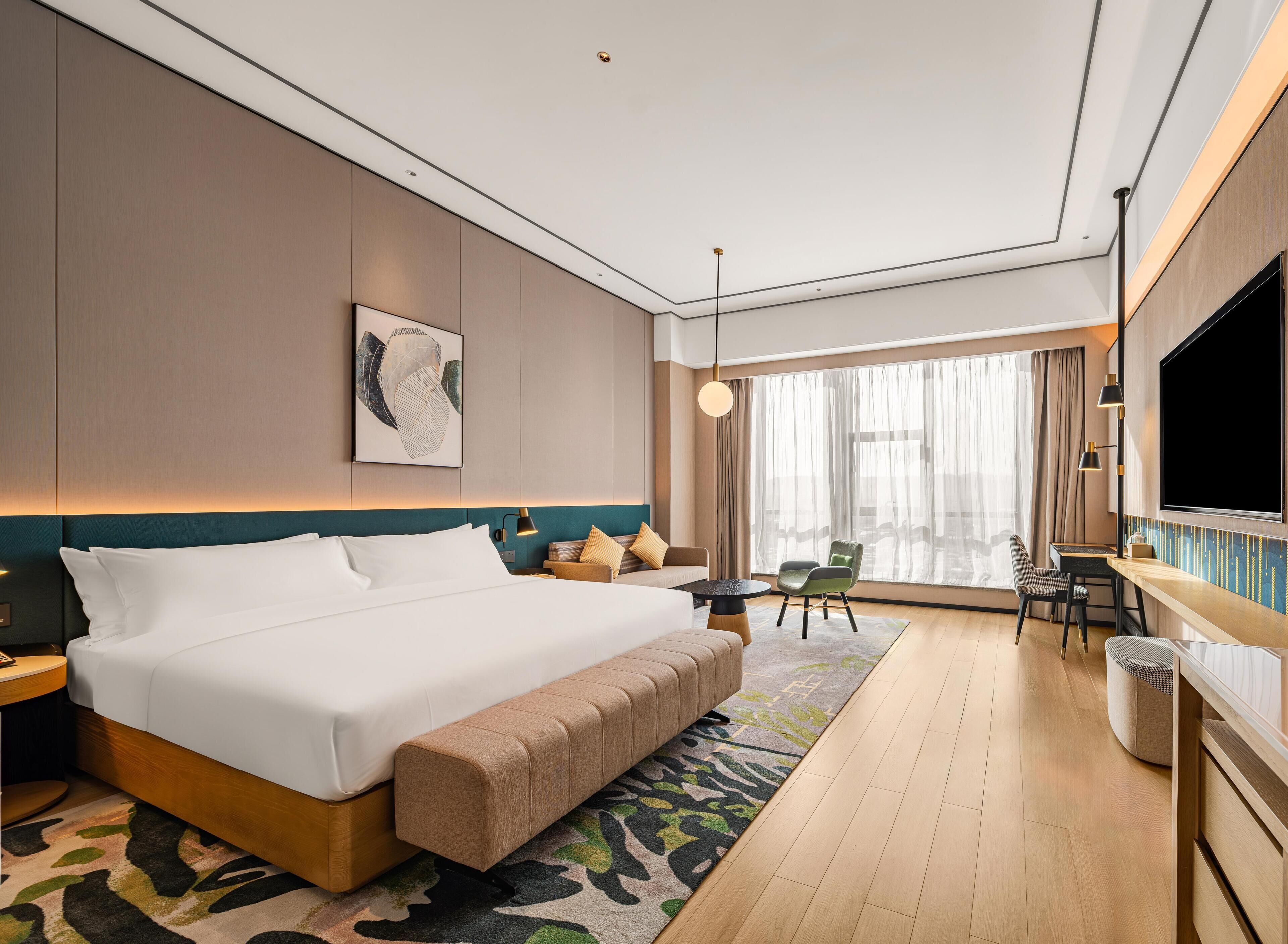 Ein modernes Hotelzimmer mit einem großen Bett, einem Schreibtisch, einem Fernseher und Blick auf die Stadt.