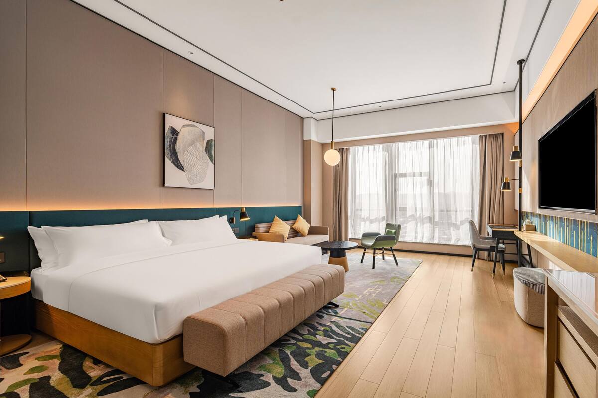 Een moderne hotelkamer met een groot bed, een bureau, een televisie en uitzicht op de stad.