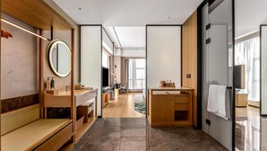 A modern hotel room with a wooden bench, a round mirror, a vanity with a television, and a desk with a chair. - Hilton Garden Inn Fenyang Yulongwan (Lvliang)