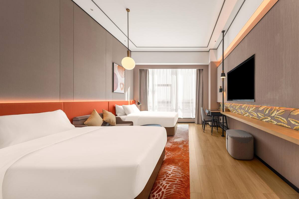 Een hotelkamer met twee bedden, een televisie, een bureau en een groot raam.