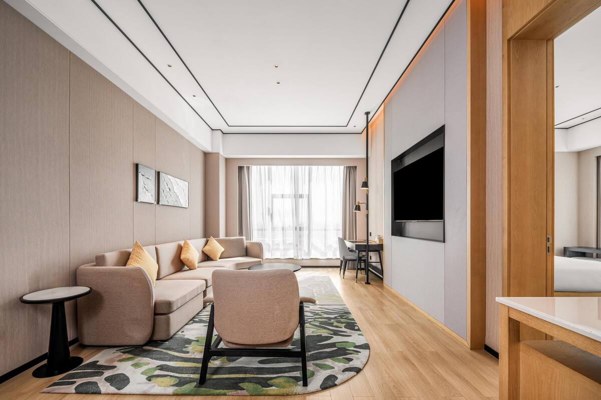 Een moderne hotelkamer met een bank, stoelen, een bijzettafeltje, een televisie en een groot raam.