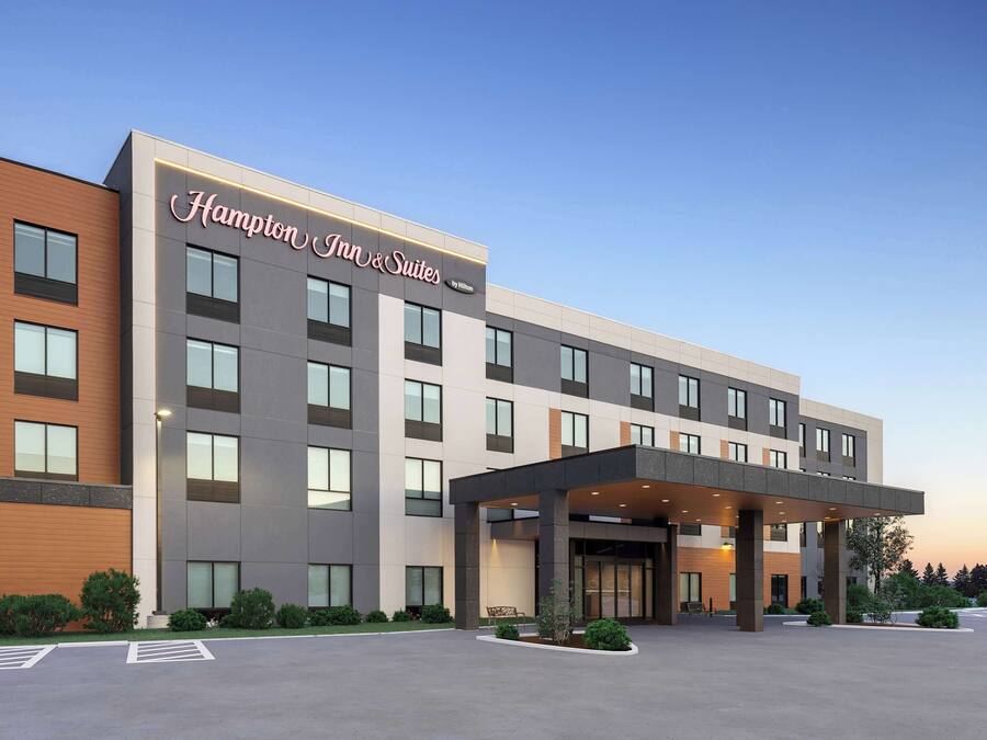 Ein Hampton Inn & Suites Hotel mit moderner Fassade, großen Fenstern und einem überdachten Eingangsbereich.