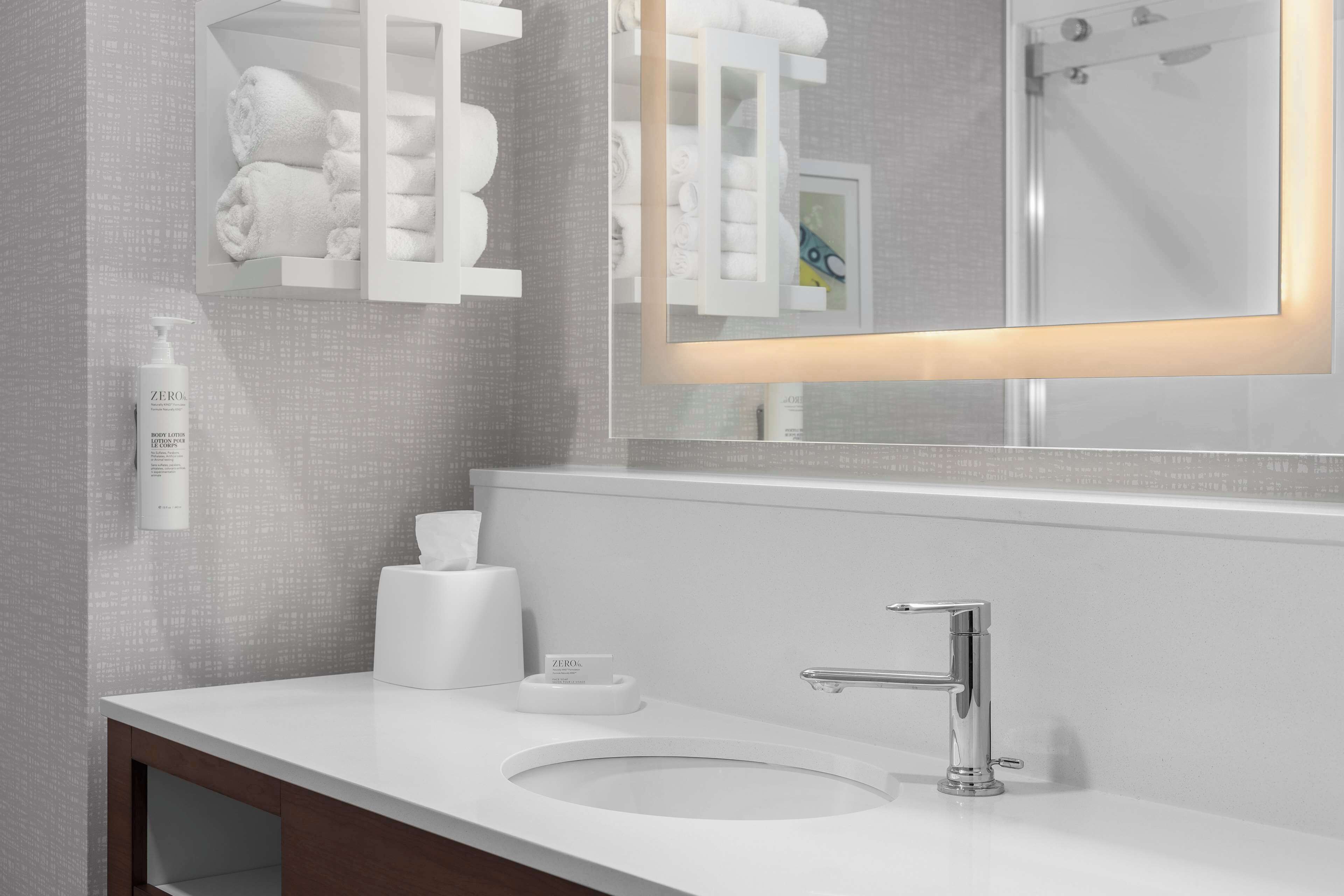 Une salle de bain moderne avec un lavabo blanc, un robinet chromé et un miroir doté d’un cadre lumineux.