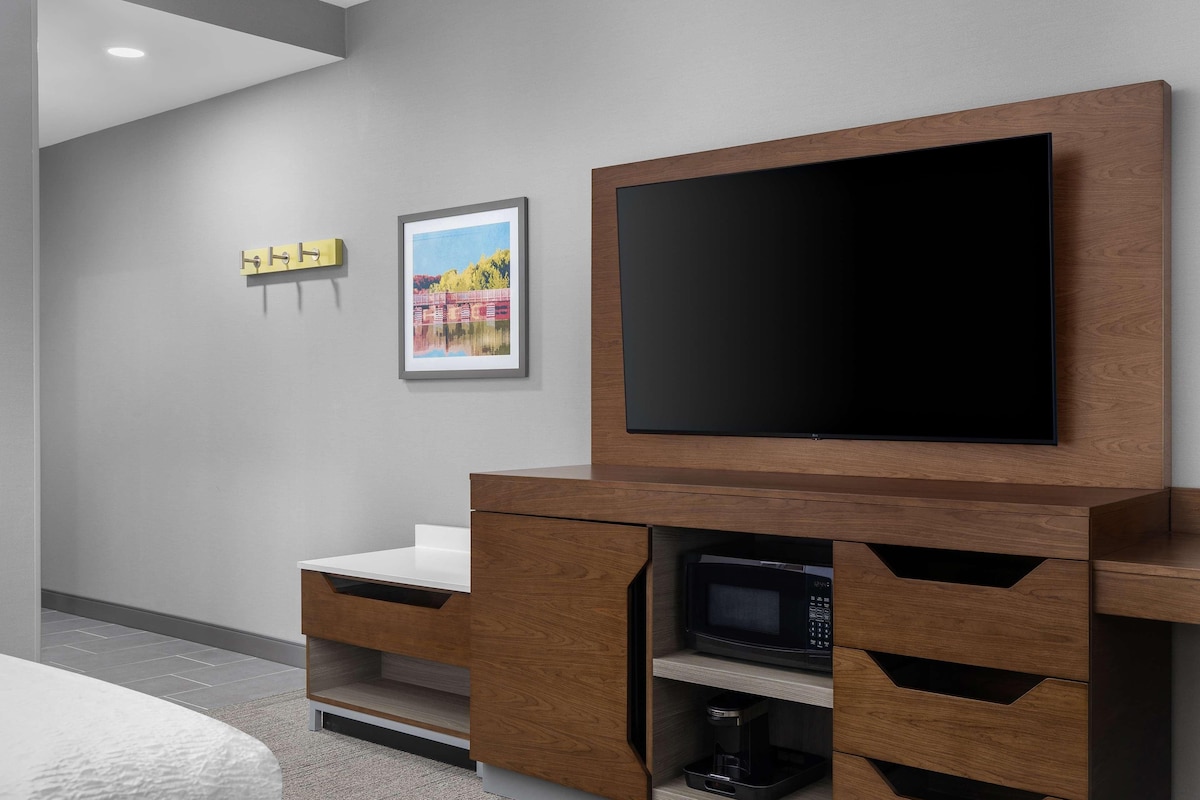 Uma sala de estar moderna com uma TV de tela plana fixada em um armário de madeira, um micro-ondas e uma pequena cafeteira.