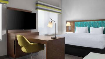 Habitación de hotel con escritorio de madera, televisor, cama con ropa blanca y ventana con cortinas.