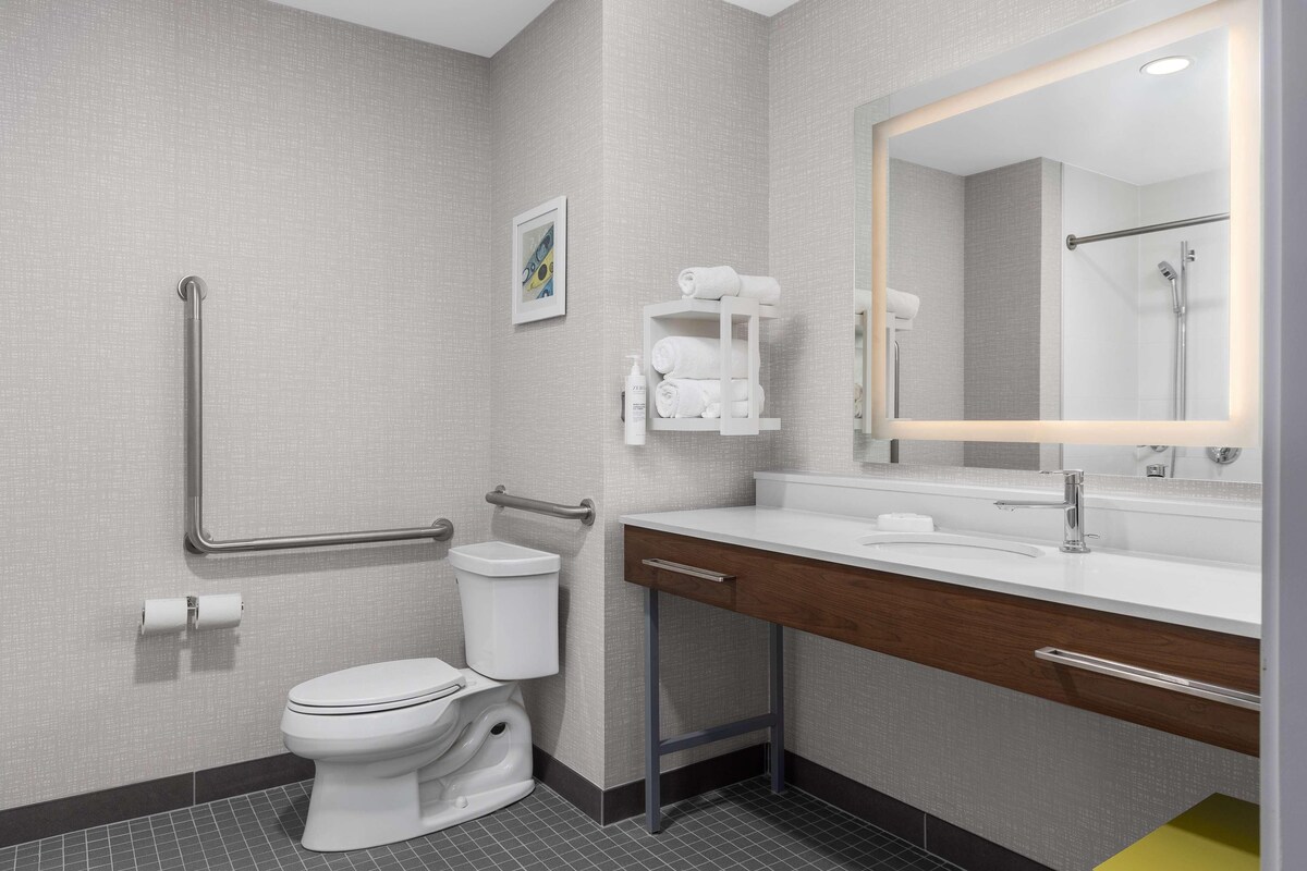 A modern bathroom with a toilet, grab bars, a sink with a mirror, and a towel rack.