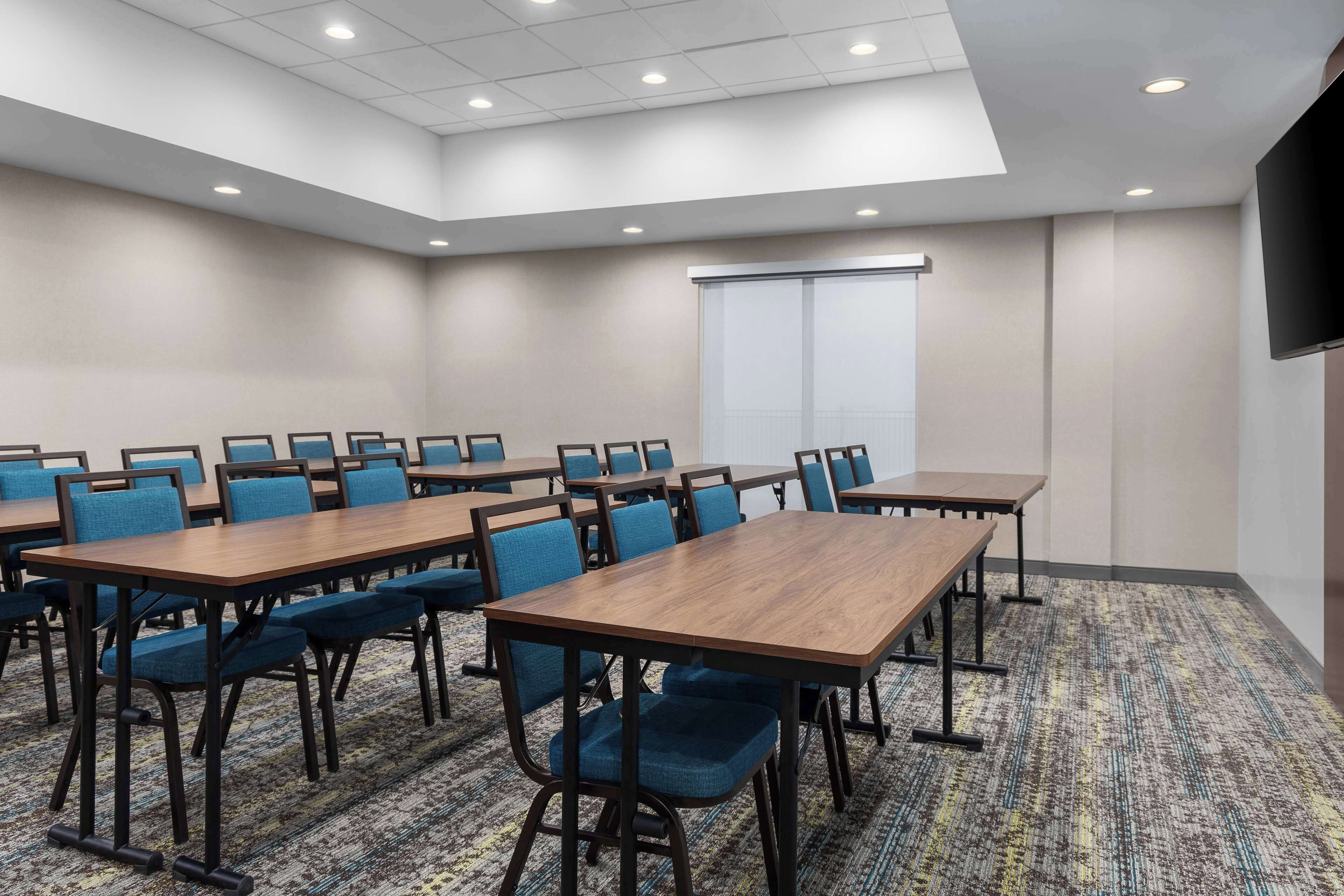 A conference room with multiple tables and chairs, a large screen, and a carpeted floor.
