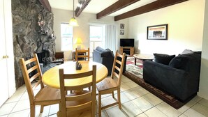 A living room with a stone wall, a wooden dining table with chairs, a sofa, a television, and a lamp. - Panorama 203 (Breckenridge)