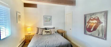 A bedroom with a bed, a nightstand, a lamp, a framed picture on the wall, and a door.