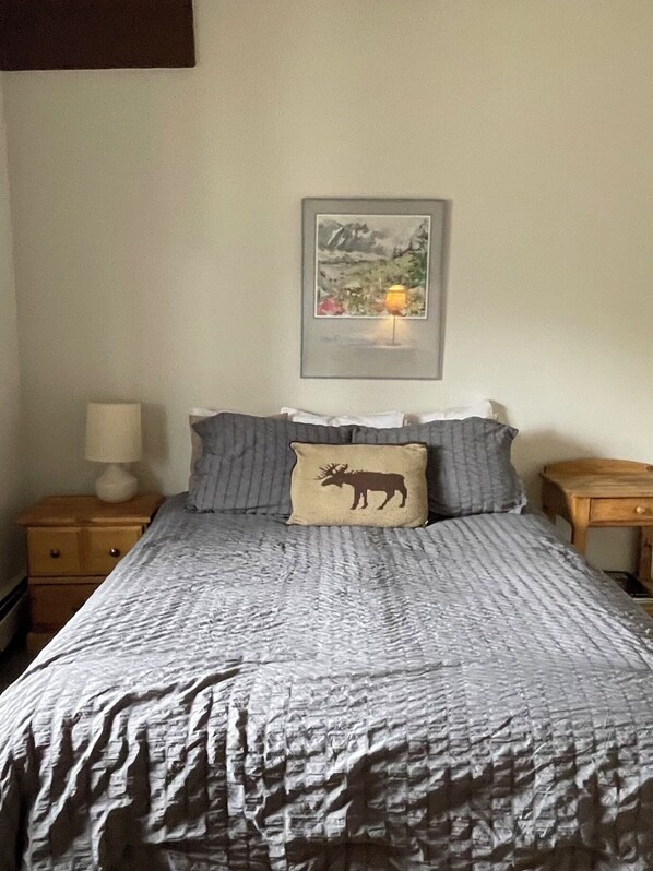 A bed with a gray and white striped bedspread, a pillow with a moose design, and a framed landscape painting above the bed. - Panorama 203 (Breckenridge)
