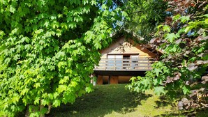 A wooden cabin with a sloped roof, surrounded by lush green foliage and a grassy area. - Chalet in the mountains, Massif du Vercors, 1100 meters, Piano at your disposal (Lans-en-Vercors)