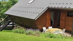 A modern house with a slanted roof, a wooden exterior, and a small patio with a table and chairs. - Chalet in the mountains, Massif du Vercors, 1100 meters, Piano at your disposal (Lans-en-Vercors)