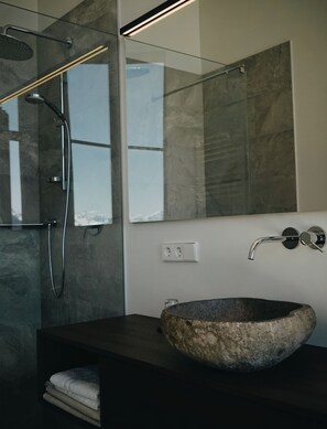 A modern bathroom with a stone sink, a glass-enclosed shower, and a large mirror. - Superb 1-Bedroom Penthouse with a View of the Dolomites (Large) (Trentino-Alto Adige)