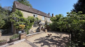 A stone house with a gravel driveway, a garden with various plants, and a small outdoor seating area. - 17th-Century Cotswold Cottage with South-Facing Orchard. (BICESTER)