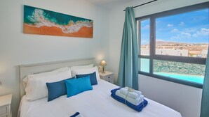 A hotel room with a bed, a nightstand, a lamp, a window with curtains, and a painting on the wall. - Casa Maria Duplex With Sea & Mountain Views (CN)