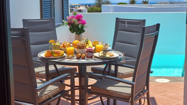A round table with four chairs, a vase with flowers, and a breakfast spread including fruits, bread, and beverages. - Casa Maria Duplex With Sea & Mountain Views (CN)