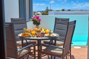 A round table with four chairs, a vase with flowers, and a breakfast spread including fruits, bread, and beverages. - Casa Maria Duplex With Sea & Mountain Views (CN)
