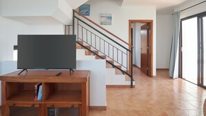A living room with a TV on a wooden stand, a staircase, and a door leading to another room. - Casa Maria Duplex With Sea & Mountain Views (CN)