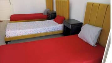 Una habitación con dos camas individuales, cada una con una colcha roja y una almohada. Hay una mesita de noche negra pequeña con una lámpara entre las camas.