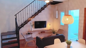 A living room with a wooden staircase, a flat-screen TV, a dining table, and a hanging light fixture. - Charming house just two minutes from the historic center of Ayamonte. (Ayamonte)