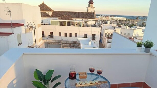 A balcony with two wicker chairs, a small table with a glass of red wine and a bottle, and a potted plant. - Charming house just two minutes from the historic center of Ayamonte. (Ayamonte)