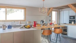 A modern kitchen with a central island, bar stools, a microwave, and a large window. - 5 bedroom Luxury chalet with panoramic view, nordic bath, high quality finis (Les Gets)