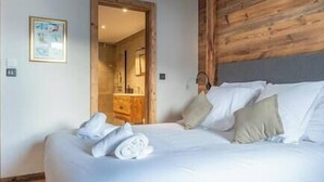 A neatly made bed with pillows and a rolled towel, a wooden headboard, and a framed picture on the wall. - 5 bedroom Luxury chalet with panoramic view, nordic bath, high quality finis (Les Gets)