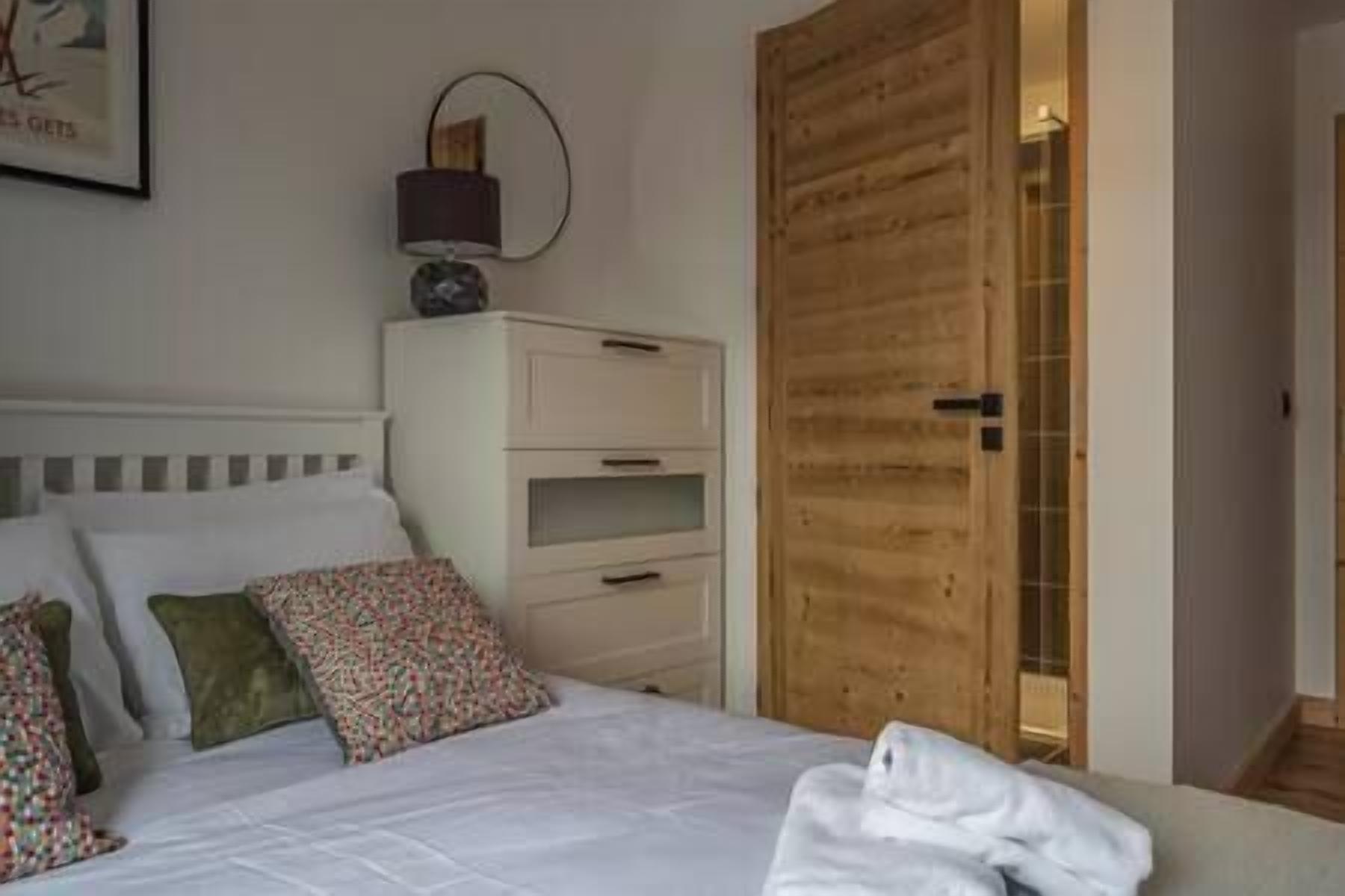 Un dormitorio con cama, almohadas, una mesita de noche y un armario de madera.