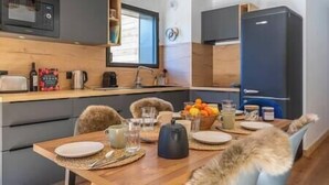 Kompakti keittiö, jossa on modernit kodinkoneet, ruokapöytä kahdelle ja ikkuna, josta tulee luonnonvaloa.
