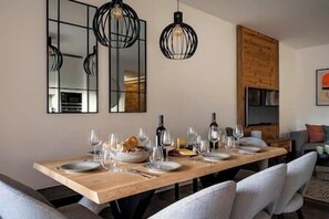 Un coin repas avec une longue table en bois dressée pour le repas, deux lampes suspendues et un grand miroir au mur.