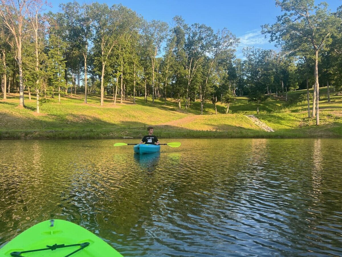 A calm lake with a kayak in the foreground and a person paddling.