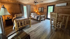 Una habitación tipo cabaña de madera con una cama de madera, una silla, una mesa, una lámpara y un ventilador de techo.