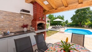 An outdoor kitchen with a brick oven, a pool, and lounge chairs.
