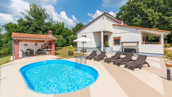 Zona junto a la piscina con piscina, sillas de descanso y área de barbacoa.