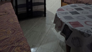Un dormitorio con televisión sobre una mesita, cama con ropa de cama estampada y ventana con persianas.