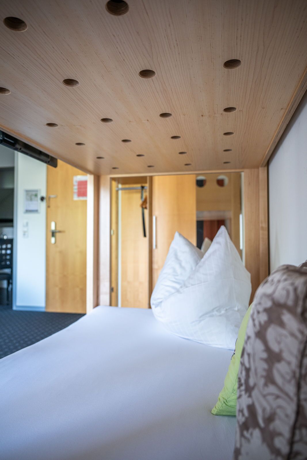 A hotel room with a wooden ceiling, a bed with white bedding, and a green pillow.