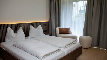 A modern bedroom with a large bed, a bedside table, a chair, and a small ottoman.