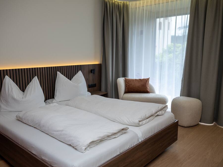 A modern bedroom with a large bed, a bedside table, a chair, and a small ottoman.