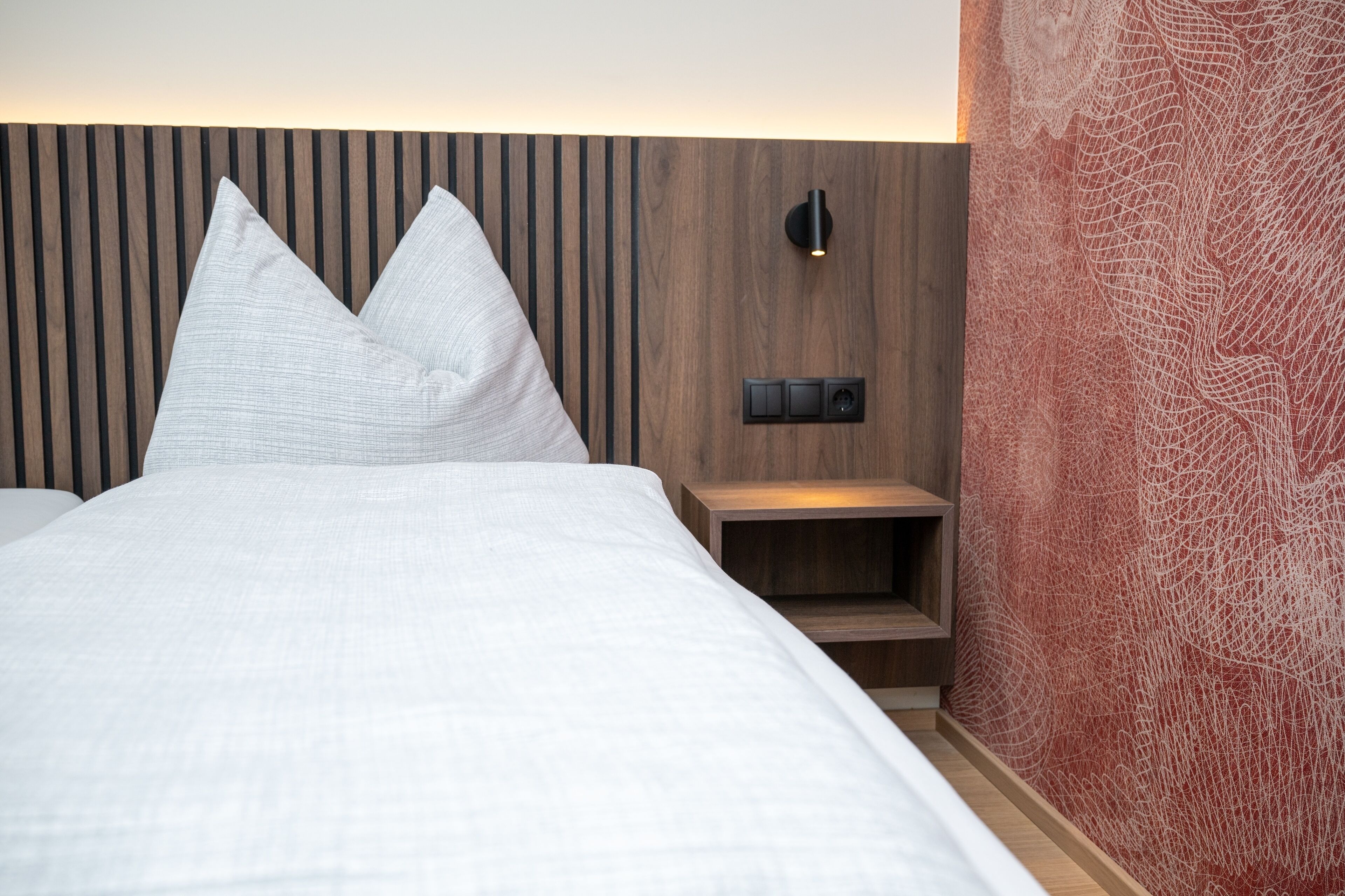 Et moderne hotelværelse med en træsenggavl, et natbord med en lampe og en rød abstrakt væg.