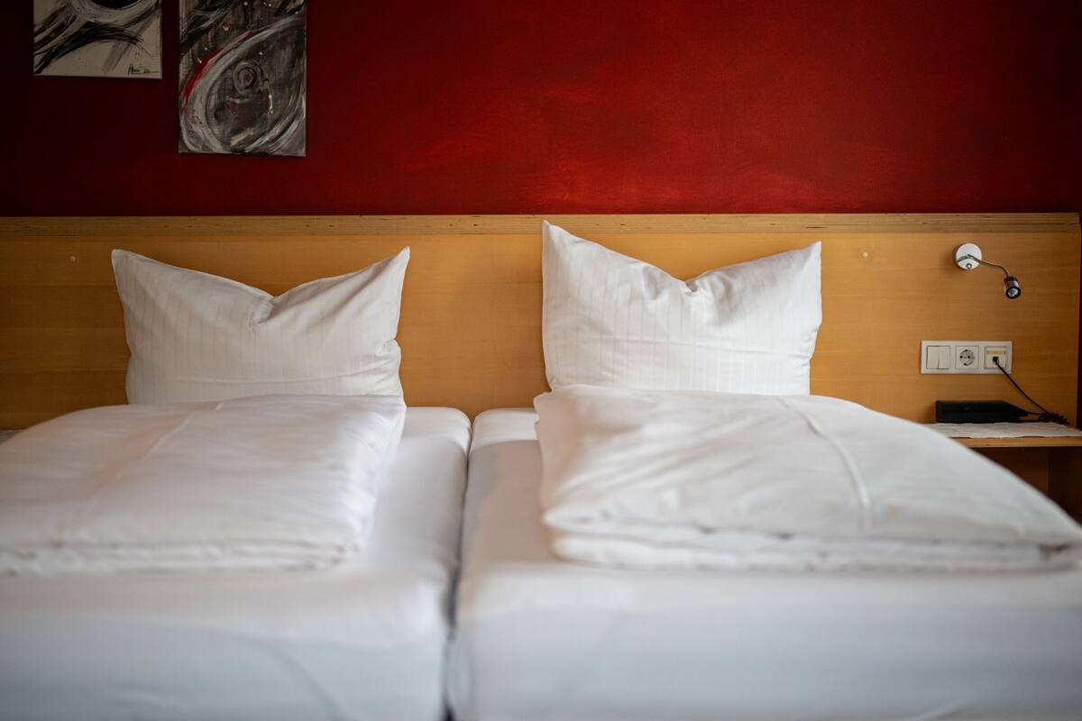 Ein Hotelzimmer mit zwei Betten, einem Holzkopfteil, einer roten Wand und einem Nachttisch mit Lampe und Telefon.