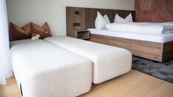 A modern hotel room with a wooden headboard, a large bed, a smaller sofa bed, and a nightstand.